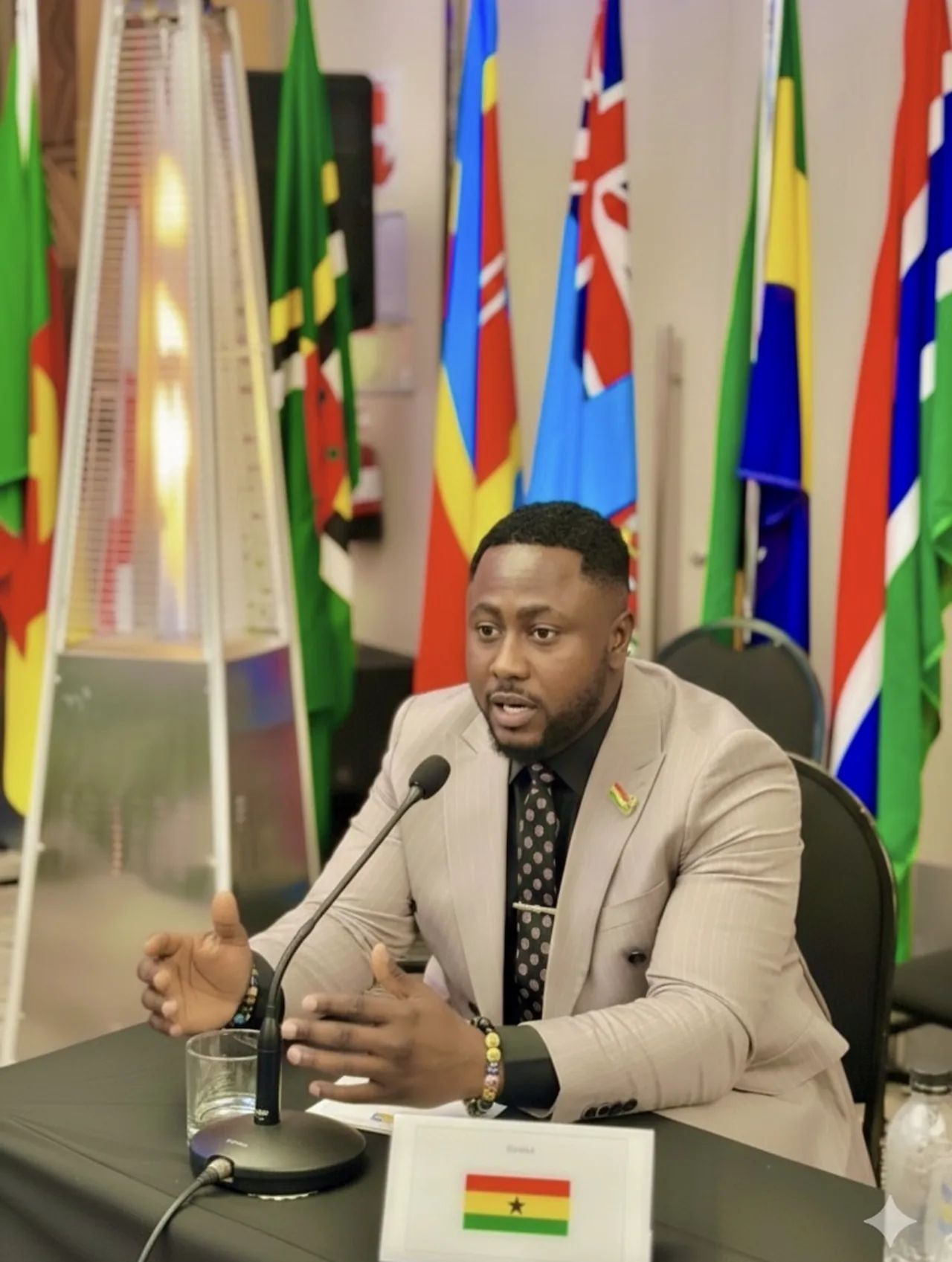 Edwin Elikem Amenyeawu speaking at the table behind Ghana's place card, national flags behind him